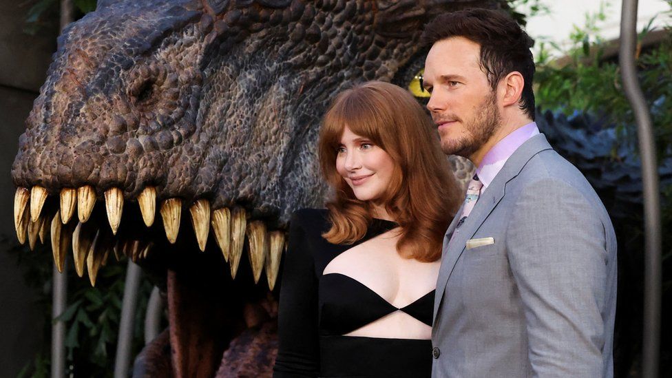 Bryce Dallas Howard and Chris Pratt posing in front of dinosaur jaws premiere for Jurassic World Dominion