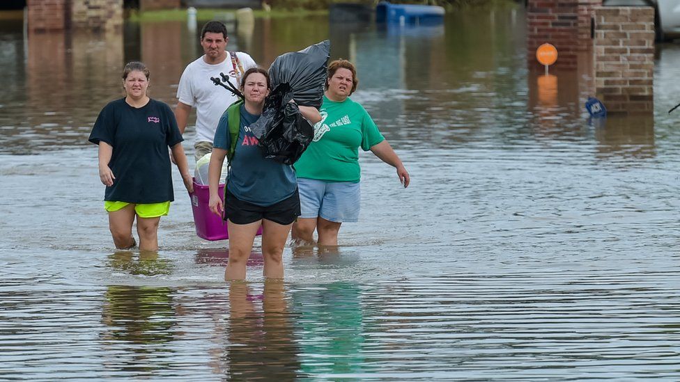 Four people wading through water that is almost up to their knees, carrying binbags and household items