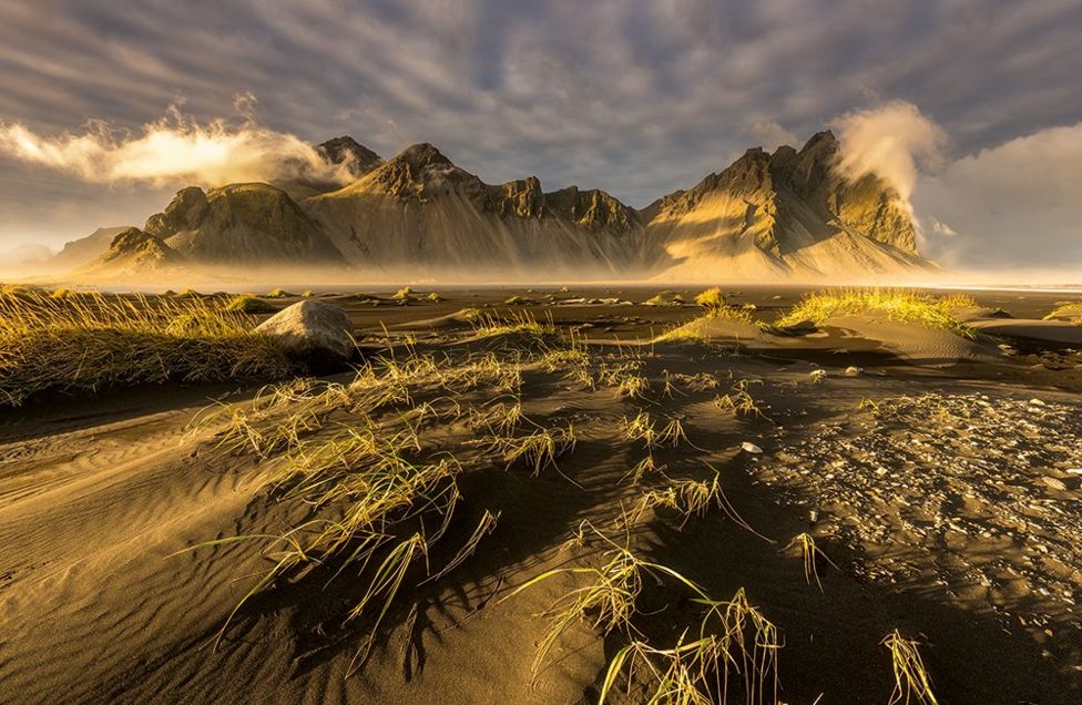 A wind-swept sandy ground with mountains in the background