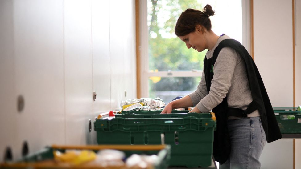 A member of staff consequentlyrts through food items inside a foodbank in Hackney, London.