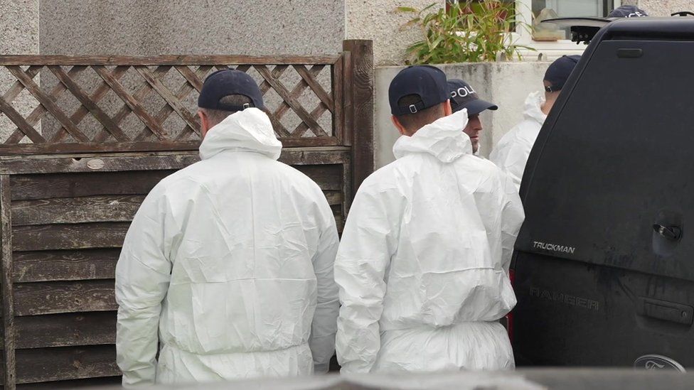 Police officers in white forensics suits with their backs turned