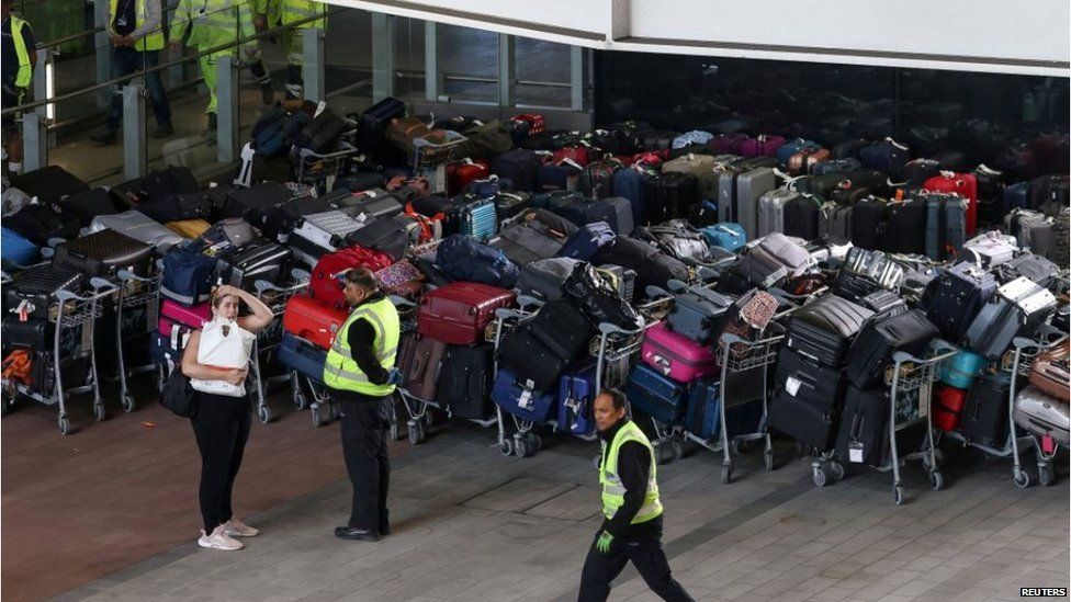 Airport workers stand next to lines of passenger luggage arranged outside Terminal 2 at Heathrow Airport. Photo taken June 19, 2022