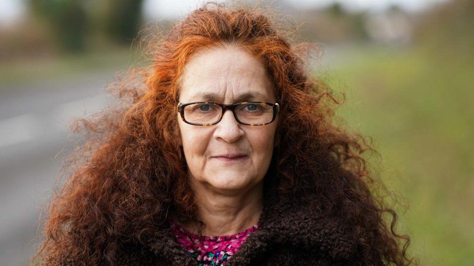 Woman with very long red hair and glasses stands by a road
