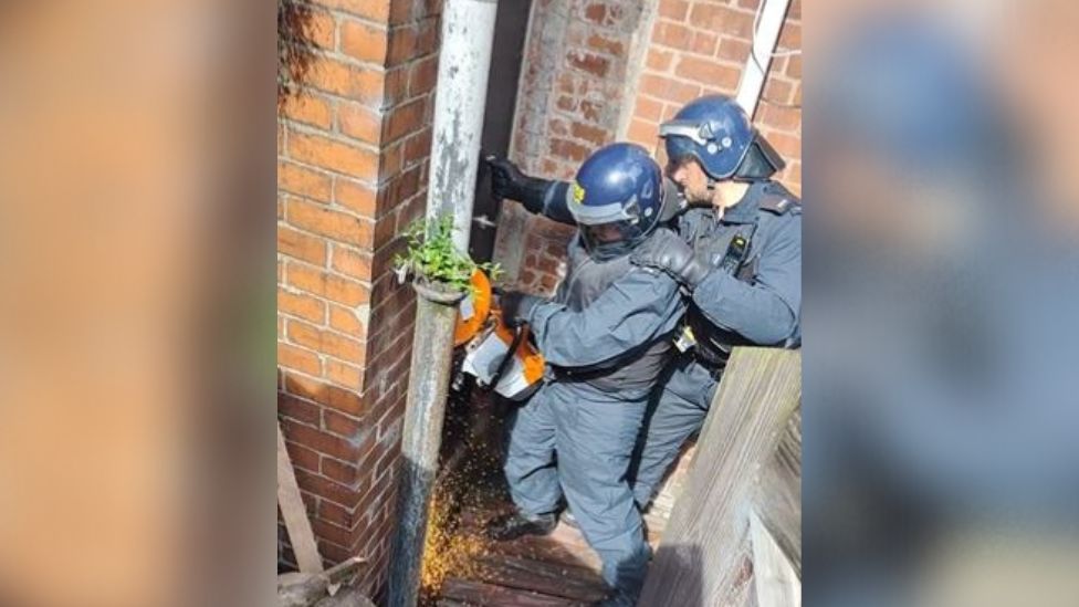 Image of police officers using a circular saw to get into a building
