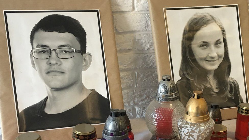 A table, covered in white linen, supports more than a dozen red candles alongside the two photos of Jan Kuciak and his fiancee Martina Kusnirova