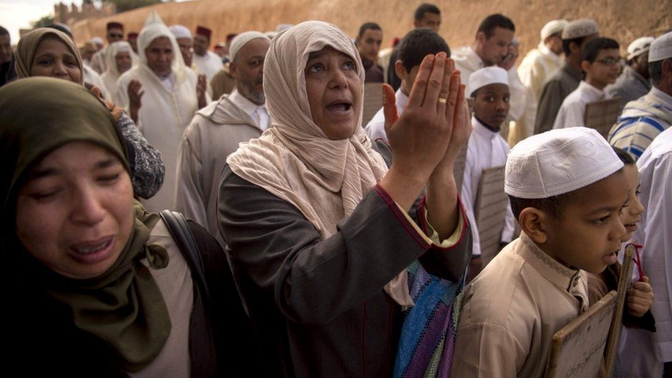 A woman looks to the sky while in a crowd praying
