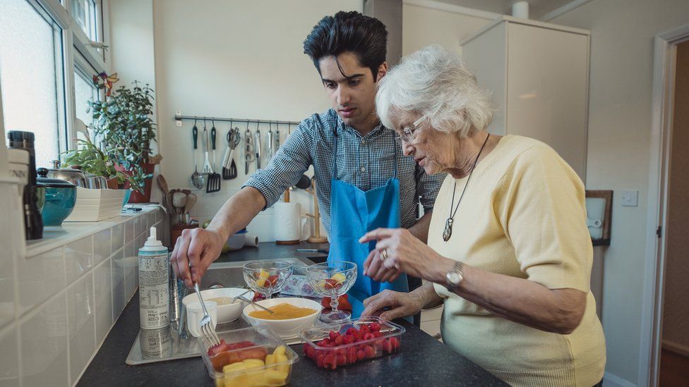 Careworker making fruit compote with an older lady in the kitchen of her home