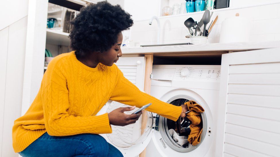 A woman places clothes inside a washing machine