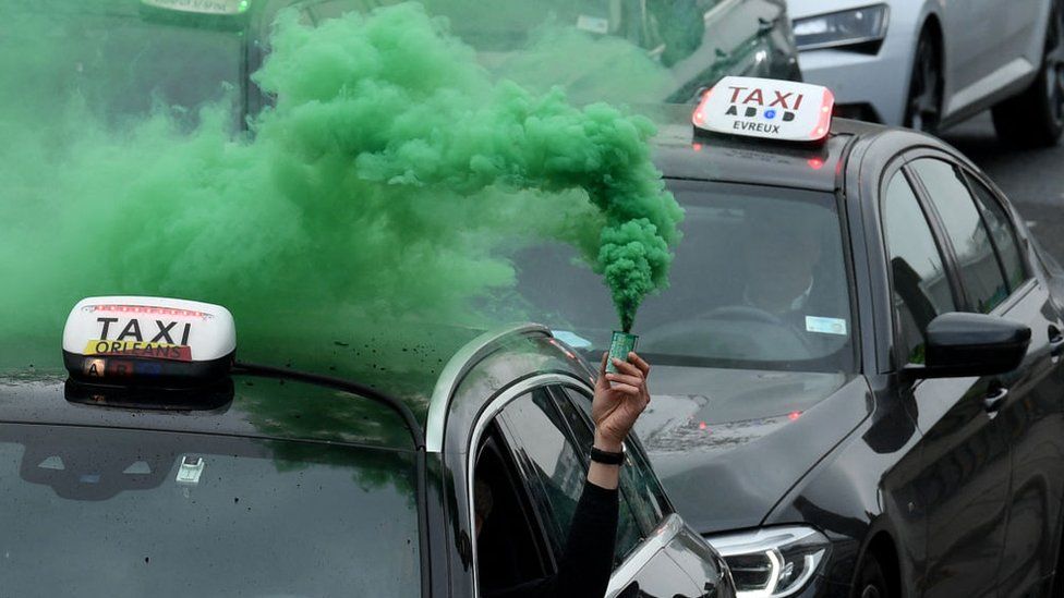 Holding a green flare out of the car window, dozens of taxis protest against a hike in fuel prices as they drive from Roissy-Charles de Gaulle airport international airport to Bercy in Paris on March 30, 2022.
