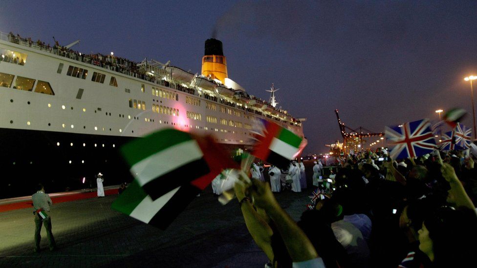 Residents of Dubai wave the British and Emirati flags as the famous cruise liner arrives at its final destination