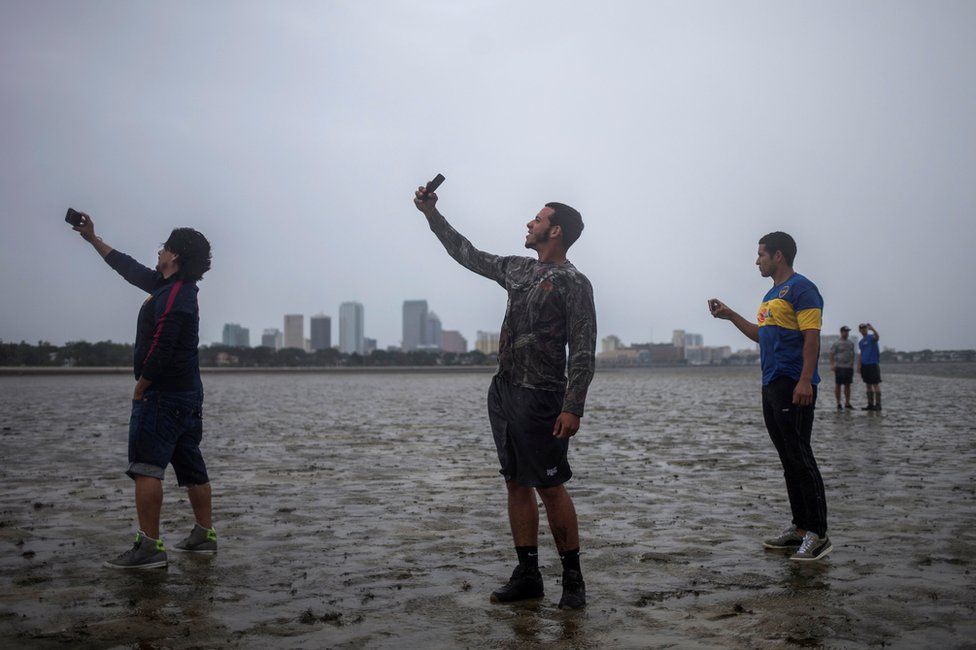 The Tampa skyline is seen in the background as local residents (L-R) Rony Ordonez, Jean Dejesus and Henry Gallego take photographs after walking into Hillsborough Bay ahead of Hurricane Irma in Tampa, Florida, 10 September