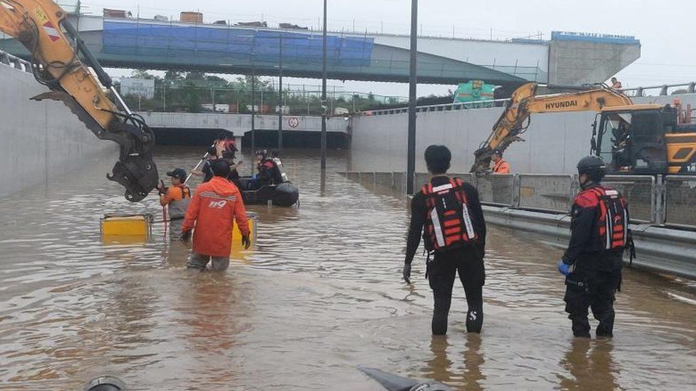 Rescuers work to reach cars trapped in a flooded tunnel in South Korea. Diggers are also seen around the entrance to the tunnel.