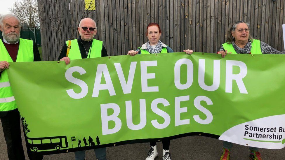 four people in hi vis holding up a green banner reading save our buses