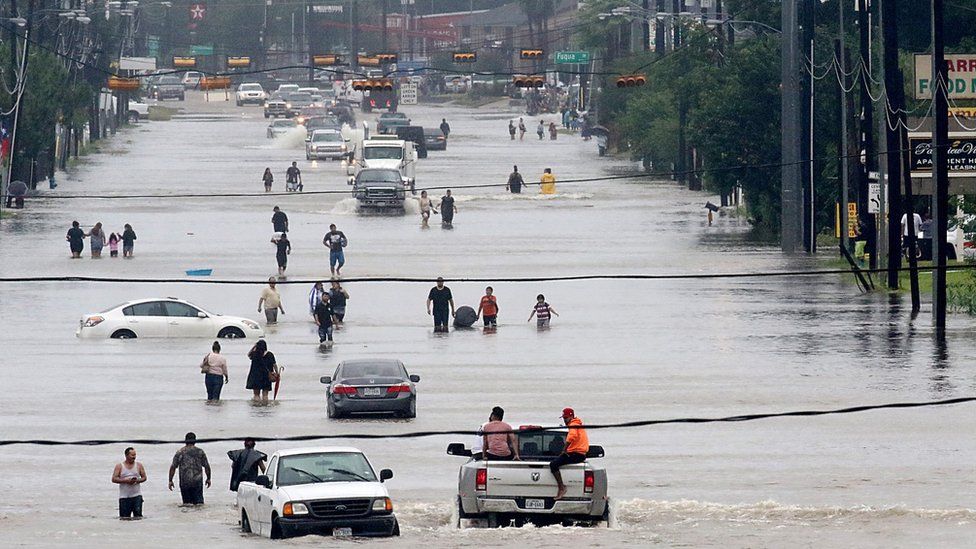 People walk through the flooded waters of Telephone Rd. in Houston on August 27, 2017 as the US fourth city city battles with tropical storm Harvey and resulting floods.