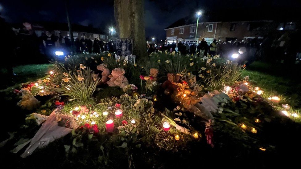 People gather around flowers left in tribute to three children who died in Sea Mills, Bristol