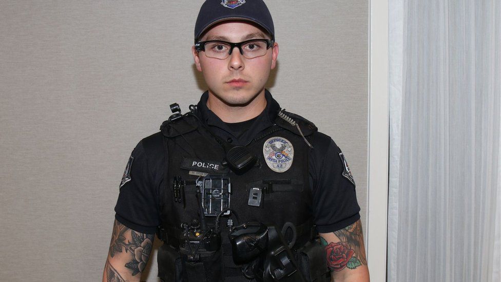 Philip Brailsford, dressed in police gear, wearing a cap and glasses. His arms are heavily tattooed and he is clean-shaven