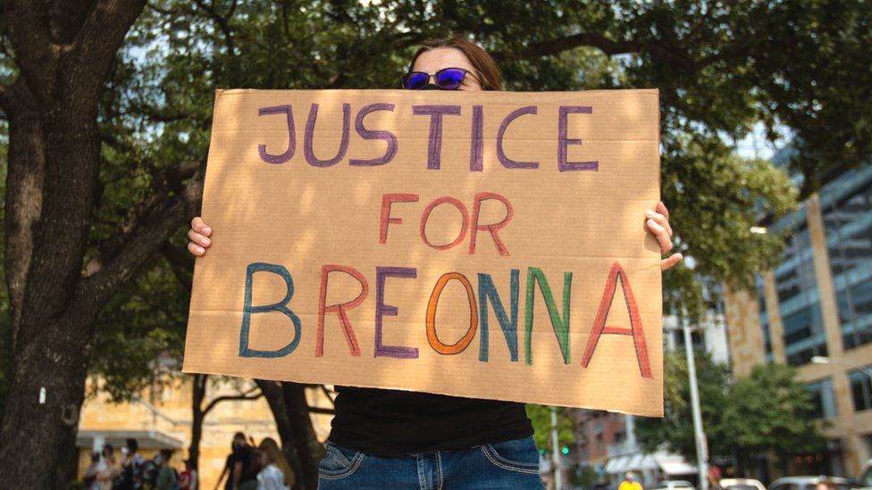 A woman holds a Justice for Breonna sign