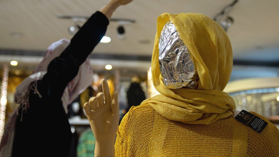 A female mannequin wearing a hijab with its face covered crudely by alfoil.