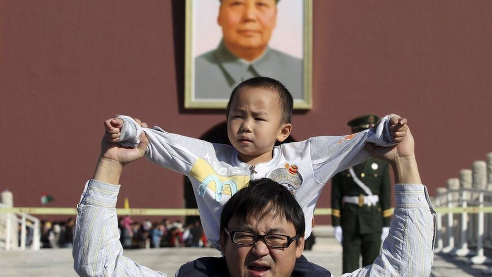 A boy sits on his father's shoulders as they pose for a photograph in front of the giant portrait of late Chinese chairman Mao Zedong on the Tiananmen Gate, in Beijing, China, October 2, 2011.