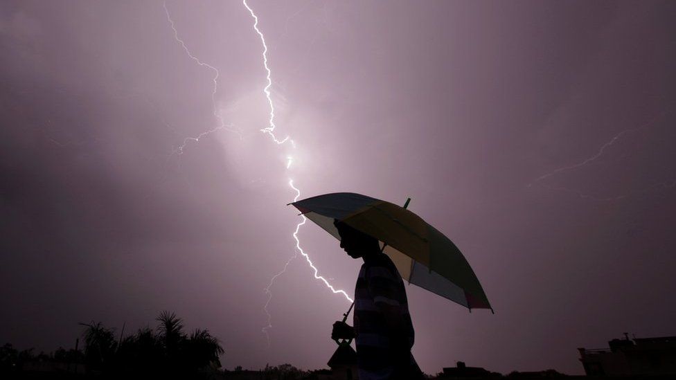 A pedestrian walks with an umbrella as lightning strikes during an evening thunderstorm in Jammu on May 14, 2015.