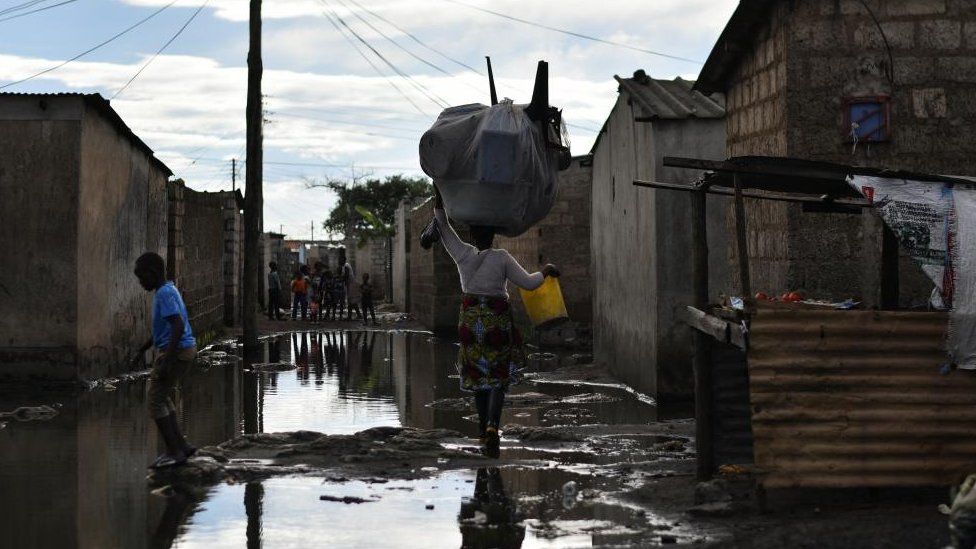 People walk across a flooded street in a neighbourhood affected by the cholera outbreak in Lusaka, Zambia January 18, 202