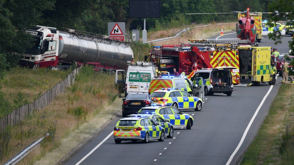 Scene of the crash with a lorry in a ditch and several emergency service vehicles, including an air ambulance, on the road