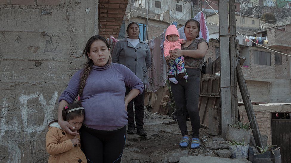 Cinthia Estrada Bolivar (31) and her three-year-old daughter stand in front of their house accompanied by their relatives.