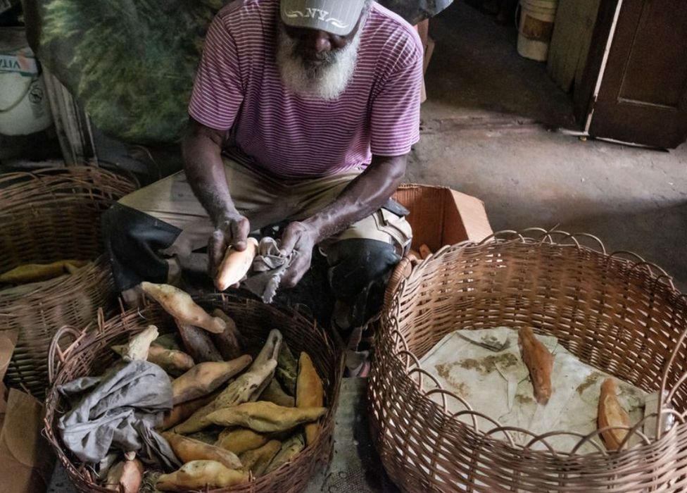A man wipes ashes from warm bread in Gray's Farm, Antigua