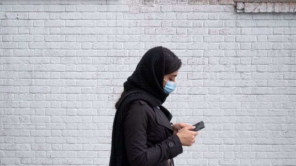 An Iranian woman uses her smartphone while walking along a street-side in northern Tehran on February 23, 2022