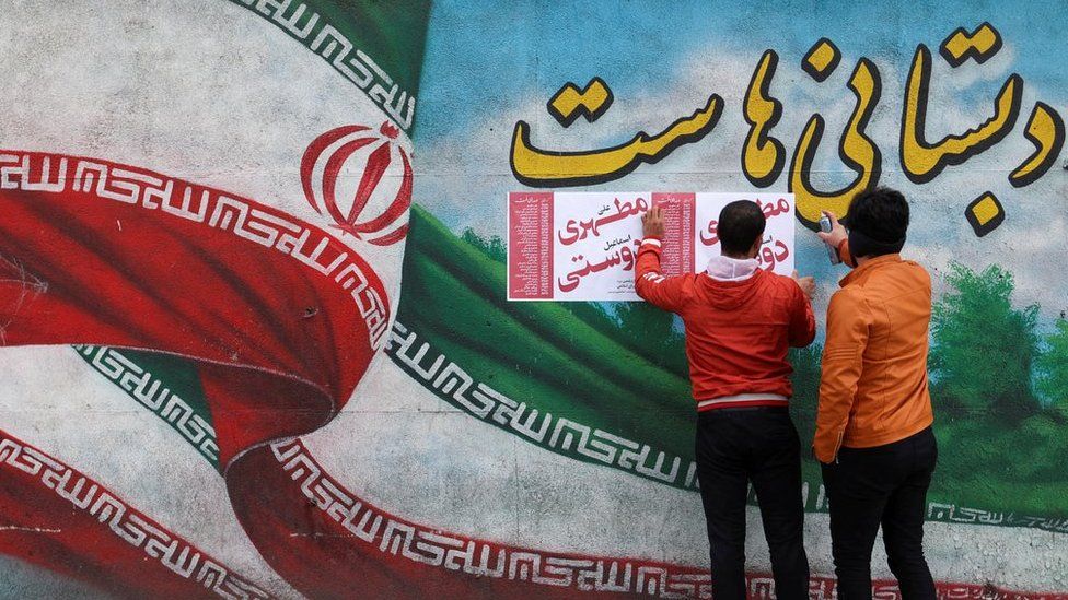 Two men put campaign posters on a wall in Tehran