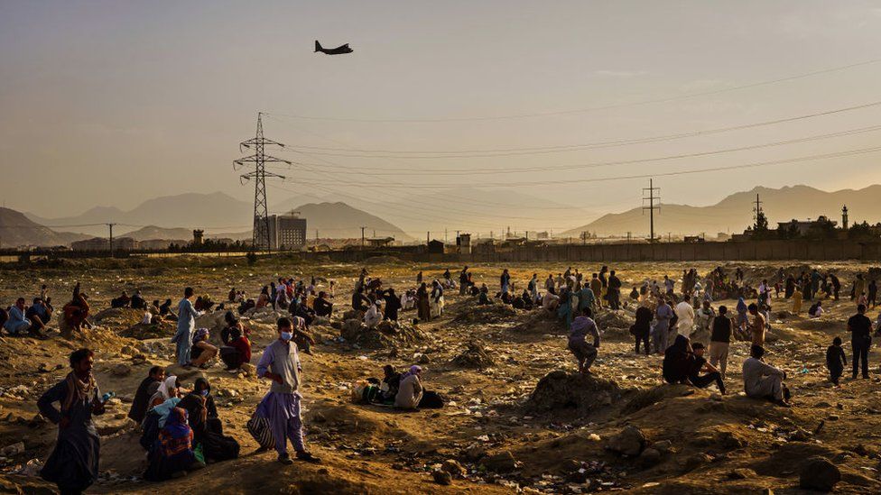 A military transport plane departs overhead as Afghans hoping to leave the country wait outside the Kabul airport on Aug. 23, 2021