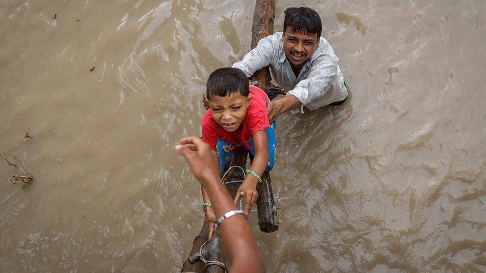 A man helps his son climb above a flooded street in Delhi
