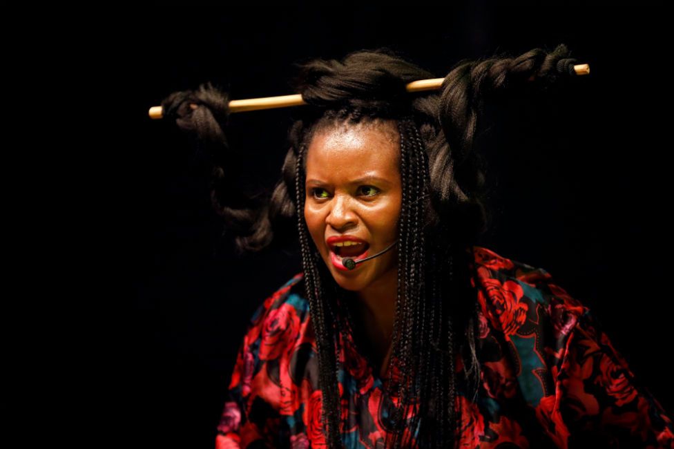 A woman sings into a microphone with her hair wrapped around a baton in an ornate style