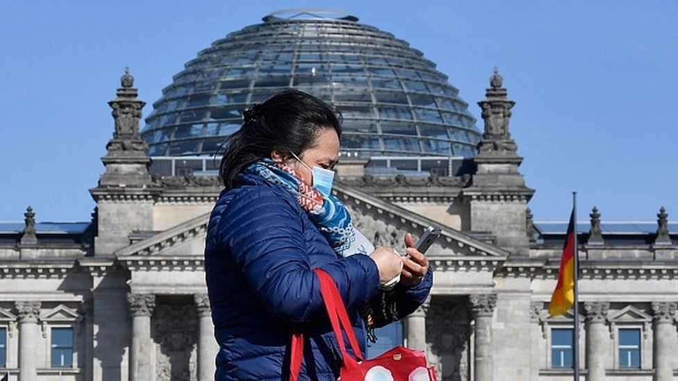 A woman wearing a face mask walks past the Reichstag building which houses the Bundestag lower house of parliament, in Berlin on April 15, 2020