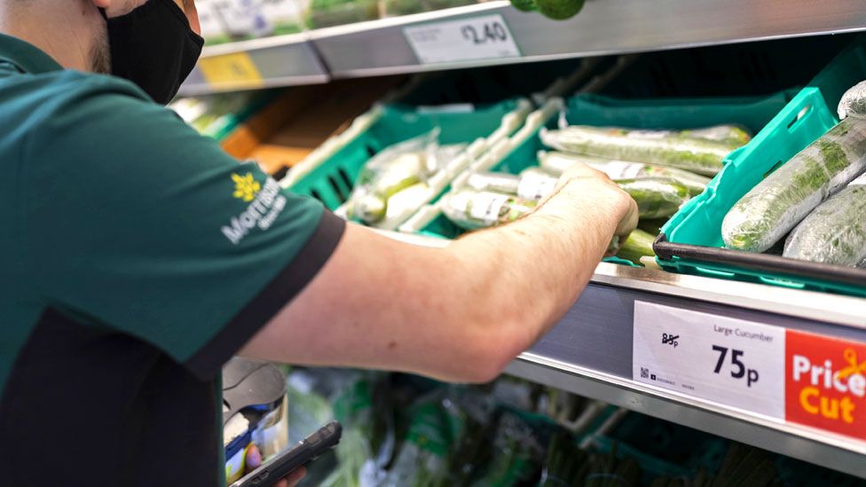 Сотрудник в форме с маской для лица сортирует свежие продукты в супермаркете Morrisons 23 августа 2021 года в Лидсе, Великобритания