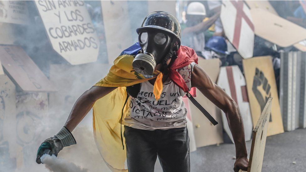man in gas mask, draped in Venezuela flag, holding a spray can