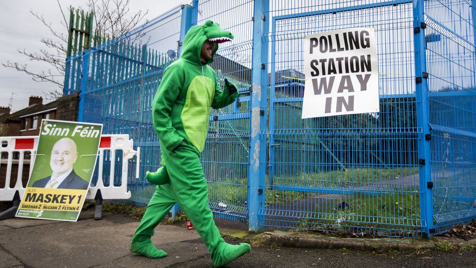 A man in a crocodile costume enters a polling station