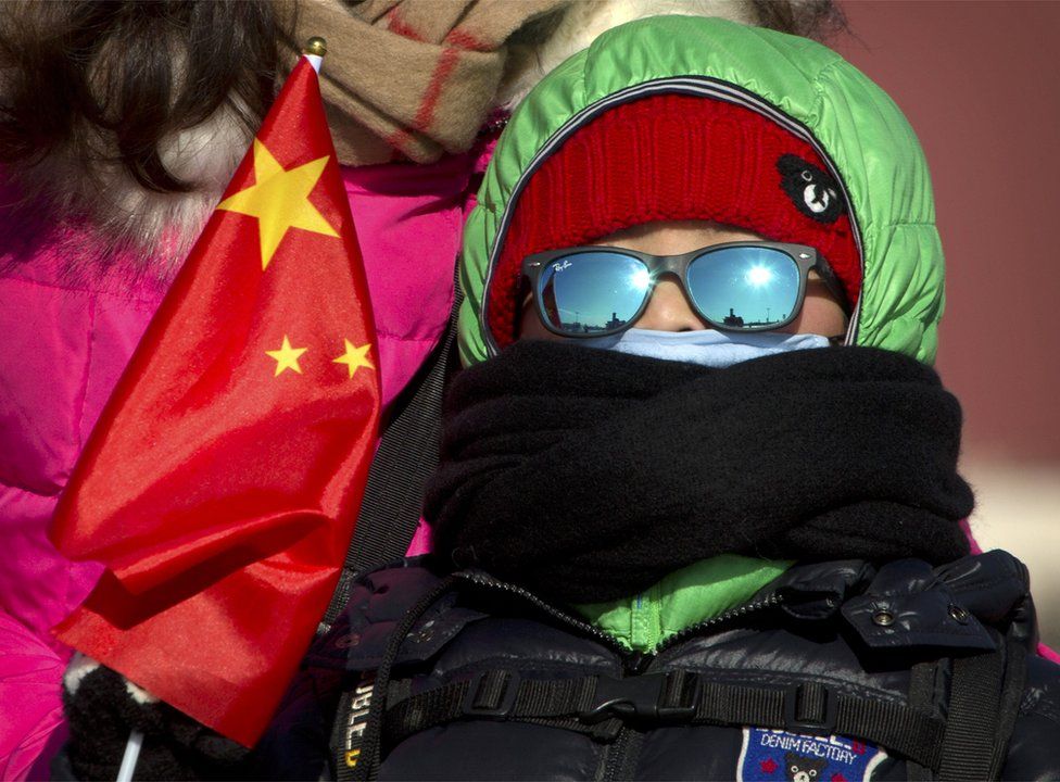A boy in heavy winter clothing holds a Chinese flag as he stands in Tiananmen Square in Beijing, Saturday, 23 January 2016