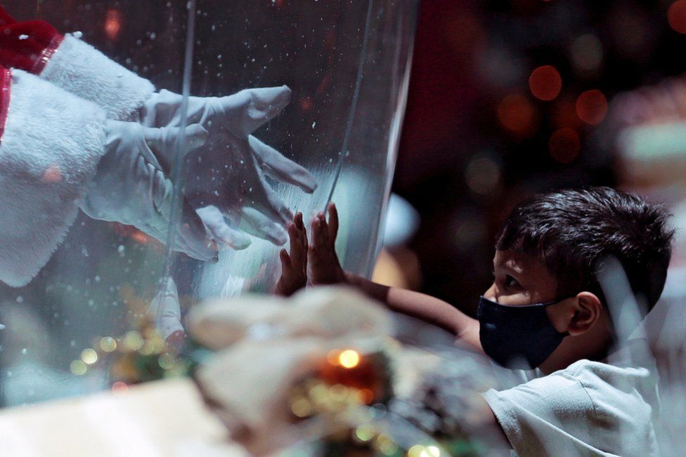 Abilio da Cruz Pinto, 77, dressed as Santa Claus inside a plastic bubble, greets a child in a shopping mall in Brasilia, Brazil, 15 December 2020