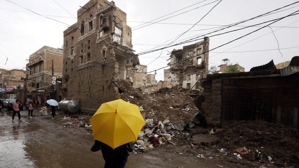 A Yemeni holding a yellow umbrella stands in front of a collapsed building in Sanaa