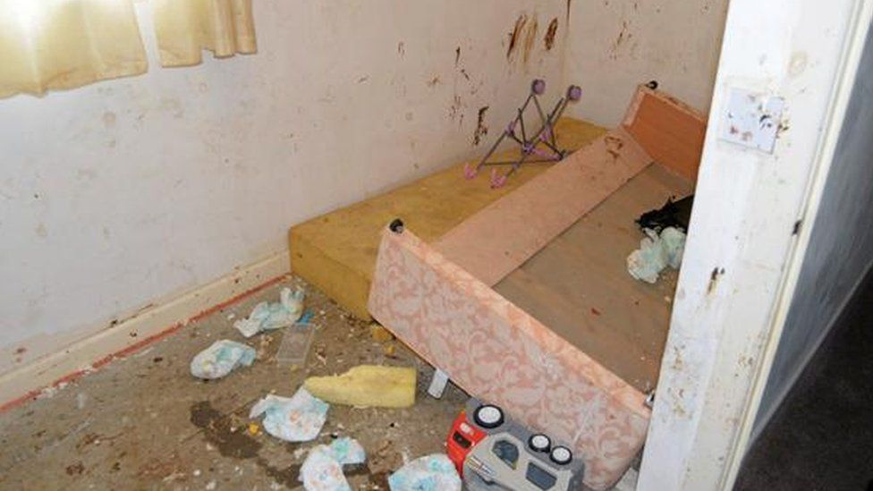 A child's bedroom with faeces on the wall and dirty nappies strewn across the floor