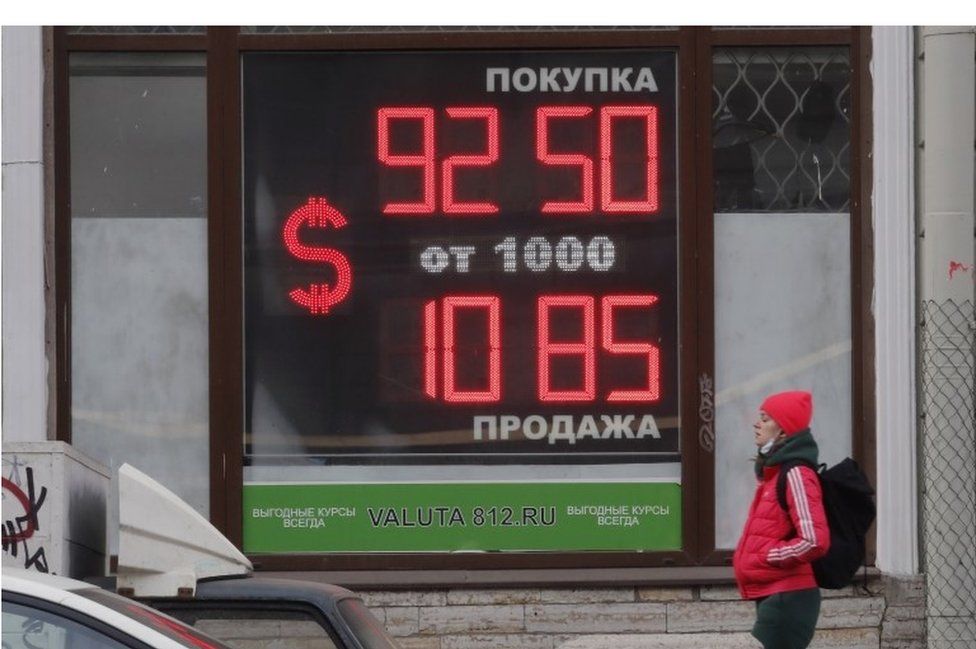 A woman walks in front of digital panel displaying the euro and US dollar currency rate at an exchange office in St. Petersburg, Russia, 28 February 2022.