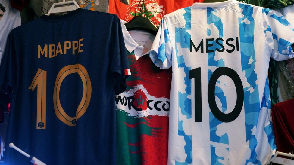 Lionel Messi and Kylian Mbappe shirts hang in a market
