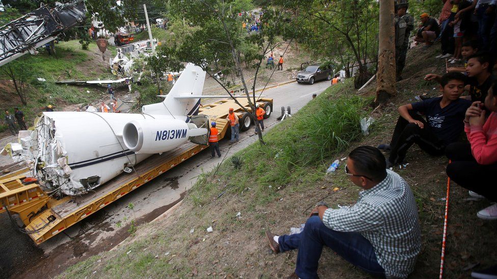 People observe a trailer transporting the wreckage of a Gulfstream G200 aircraft that skidded off the runway