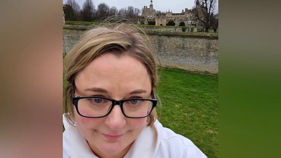 Woman with fair hair and glasses stands in front of a stately home