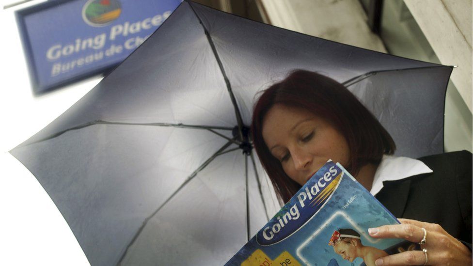 A lady contemplates getting away from the rain outside a Going Places store in London; part of the Thomas Cook Group.