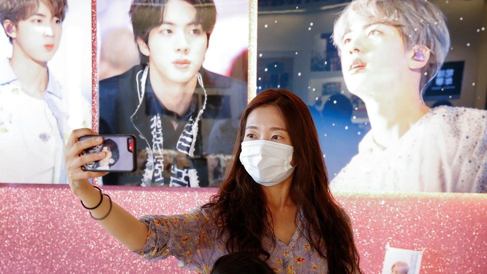 A fan of K-pop boy band BTS takes a selfie at a cafe decorated with photos and merchandise of them, in Seoul.
