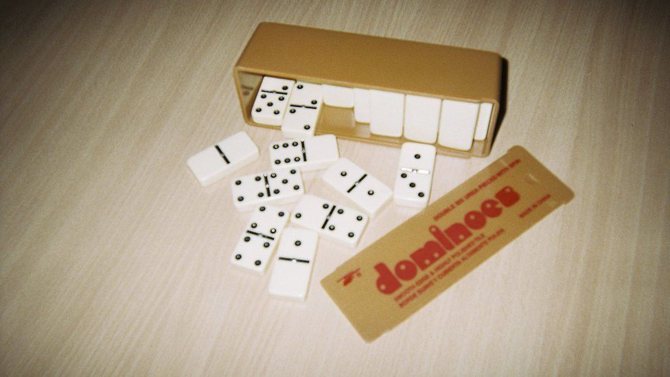 A dominoes box on its side with dominoes tumbling out