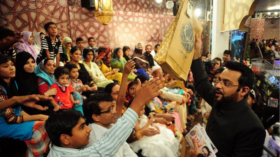 Pakistani television show host Aamir Liaquat Hussain (R) distributes gifts to the audience during an Islamic quiz show
