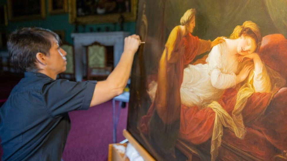 A paintings conservator works on an oil painting depicting two women